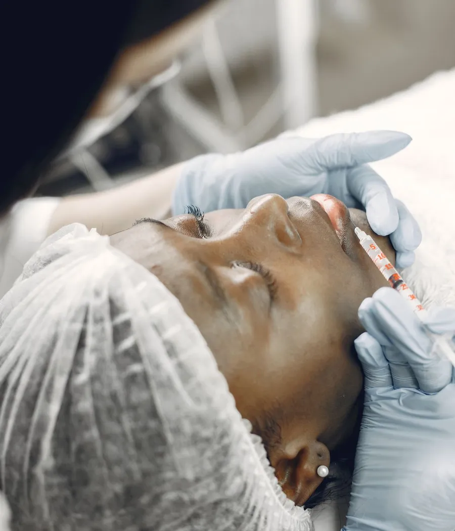 Profissional de luvas fazendo uma aplicação próxima aos lábios de uma paciente negra