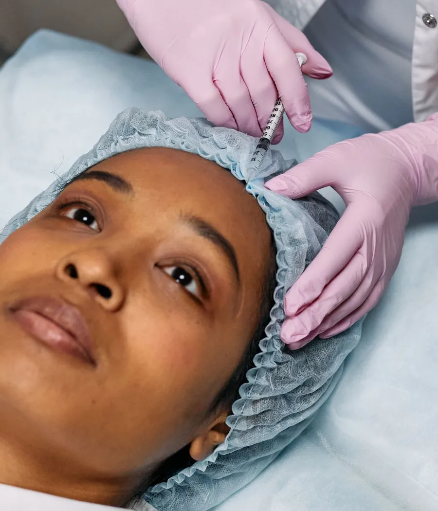 Profissional aplicando toxina botulínica na testa de uma paciente negra