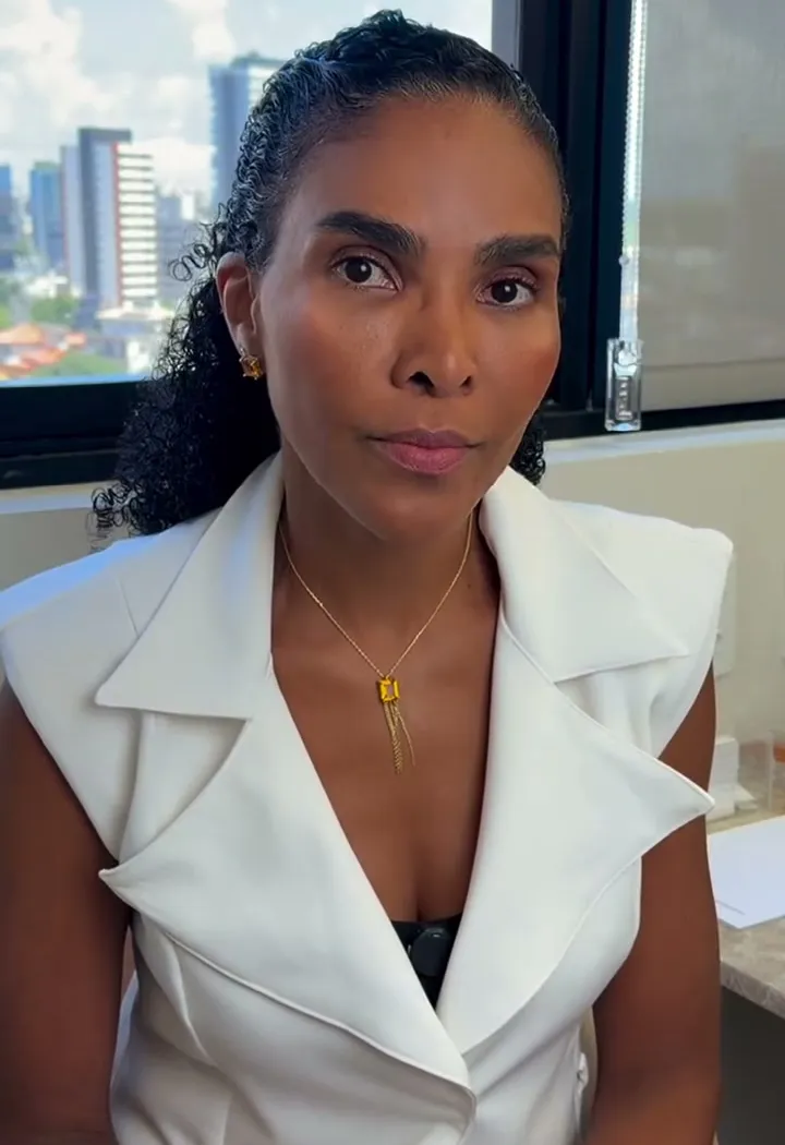 Dra. Rosana Frempong gravando vídeo no consultório, com a cidade ao fundo pela janela
